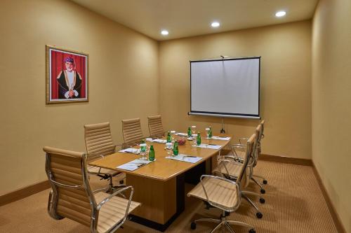 サラーラにあるSalalah Gardens Hotel Managed by Safir Hotels & Resortsのテーブルと椅子とスクリーンを備えた会議室