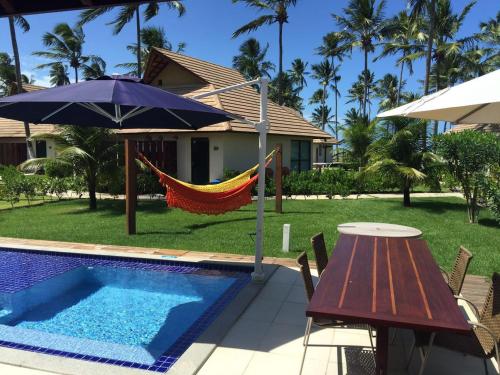 uma rede de descanso junto a uma piscina com mesa e guarda-sol em Bangalô luxo Carneiros Beach Resort em Praia dos Carneiros