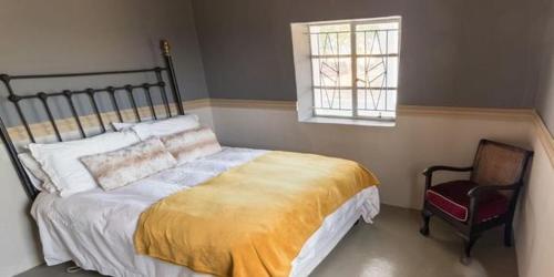 a bedroom with a bed and a chair and a window at Volmoed Cottage in Oudtshoorn