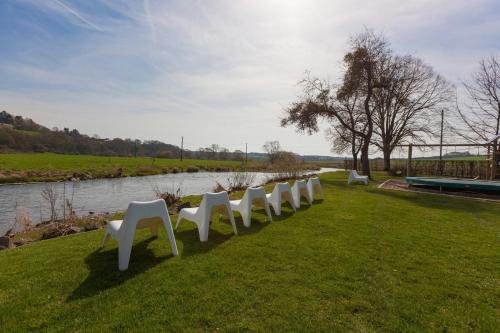 a row of white chairs on the grass near a river at Hotel La Passerelle in Grandhan
