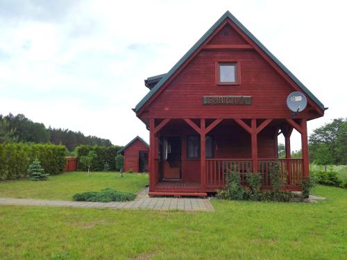 a red building with a porch in a field at Domek Sabrinka in Słajszewo