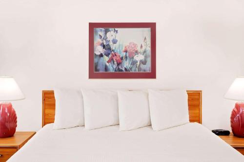 a white bed with white pillows and a painting on the wall at Baymont by Wyndham St. Joseph/Stevensville in Stevensville