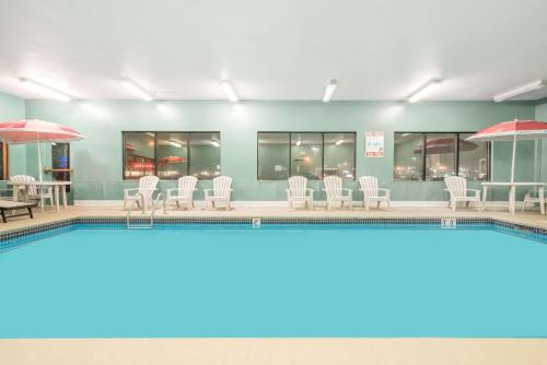 a swimming pool with white chairs and umbrellas at Baymont by Wyndham Eau Claire WI in Eau Claire