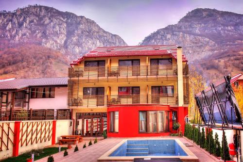 a building with a swimming pool in front of a mountain at Pensiunea JOJO in Băile Herculane