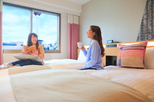 duas raparigas sentadas em camas num quarto de hotel em Kyoto Tower Hotel Annex em Quioto