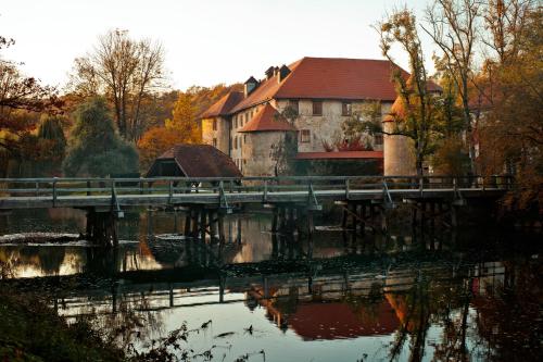 eine Brücke über einen Fluss mit einem Gebäude und einem Haus in der Unterkunft Hotel Grad Otočec - Relais Chateaux in Otočec