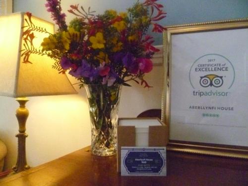 a vase of flowers sitting on a table next to a clock at Aberllynfi Riverside Guest House in Glasbury