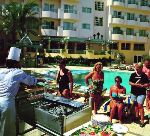 a group of people standing around a grill next to a pool at Sea Garden Hotel in Hurghada