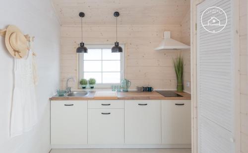 a kitchen with white cabinets and a window at Pastelowe Domki Darłówko in Darłówko