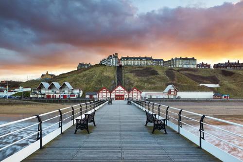 a wooden pier with benches on a beach with buildings at OutRam 26 in Stockton-on-Tees