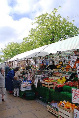 a market with people standing in front of a fruit stand at OutRam 26 in Stockton-on-Tees
