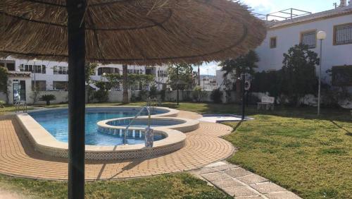 a swimming pool with a straw umbrella next to a building at Casa Verano in Vistabella