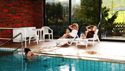 three women sitting in chairs by a swimming pool at Hotel Wiesengrund in Lindenfels