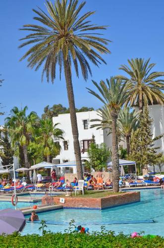 a swimming pool with palm trees and people in a hotel at Caribbean Village Agador - All inclusive in Agadir