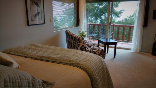 ein Schlafzimmer mit einem Bett und einem Stuhl sowie einem Balkon in der Unterkunft Greenhouse Inn by the Bay in Sequim