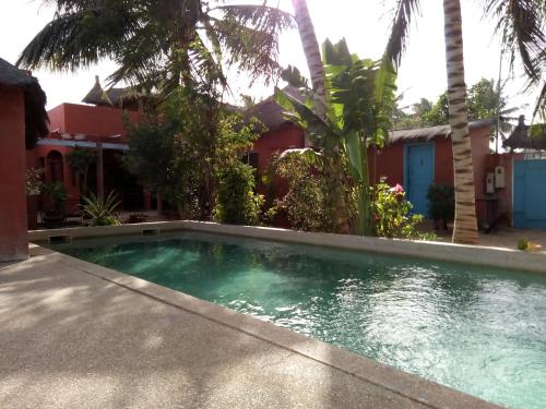 una piscina di fronte a una casa con palme di Hôtel Joal Lodge a Joal-Fadiout