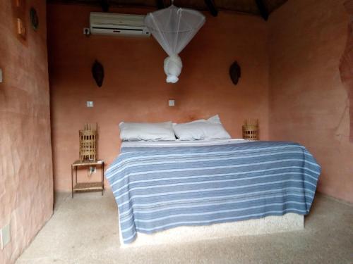 a bedroom with a bed with a blue and white striped blanket at Hôtel Joal Lodge in Joal-Fadiout