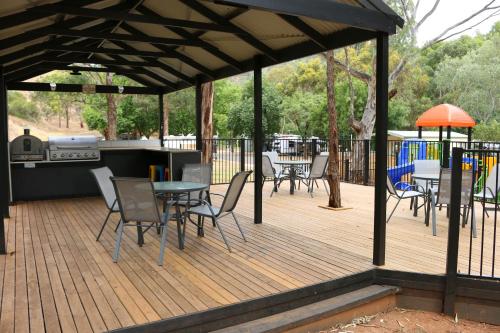 a wooden deck with chairs and tables and a grill at Adelaide Brownhill Creek Tourist Park in Adelaide