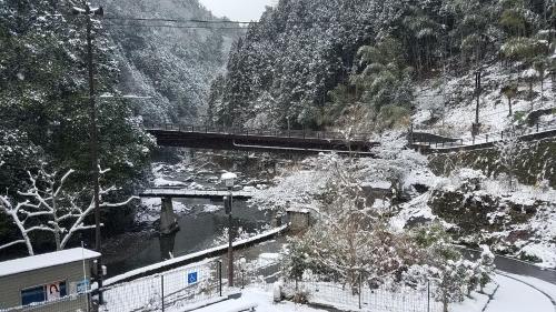 a bridge over a river with snow on a mountain at Yadori Onsen Iyashinoyu in Hashimoto