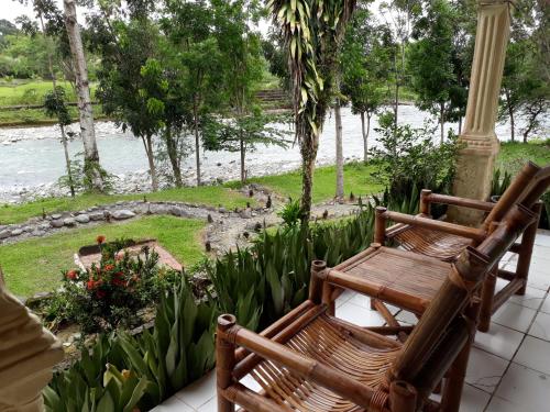 two wooden benches sitting on a porch overlooking a river at Wisma Batu Mandi in Bukit Lawang
