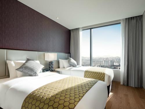 two beds in a hotel room with a large window at Grand Mercure Ambassador Hotel and Residences Seoul Yongsan in Seoul