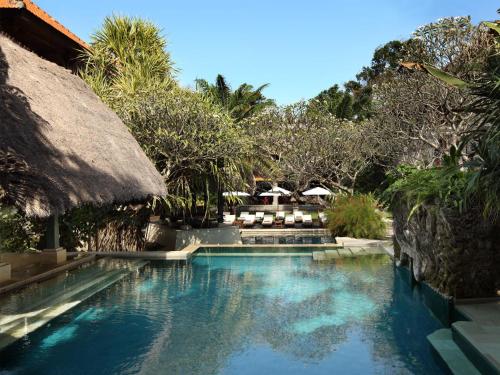 a swimming pool at a resort with trees and chairs at Puri Santrian Beach Resort And Spa in Sanur