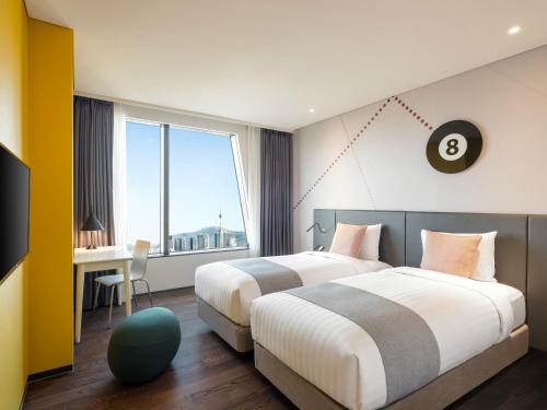 a hotel room with two beds and a desk and a window at ibis Styles Ambassador Seoul Yongsan in Seoul