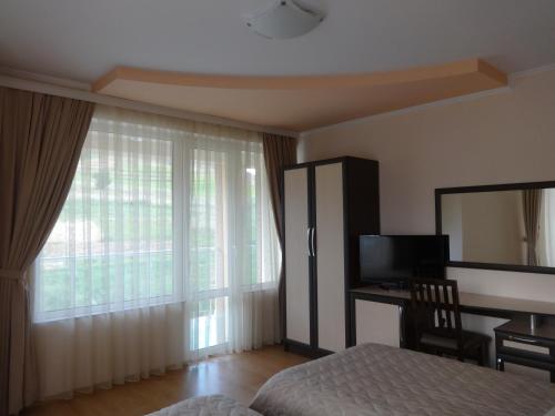 a bedroom with a bed and a desk and a window at Семеен хотел "Елеганс" - Борино in Borino
