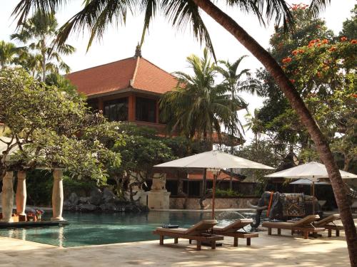 a resort with a swimming pool with benches and umbrellas at Puri Santrian Beach Resort And Spa in Sanur