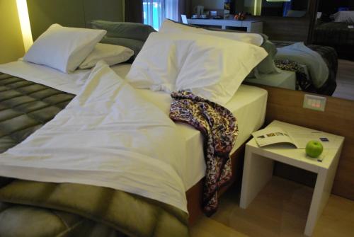 a bed with white sheets and a table with a book at Idea Hotel Plus Savona in Savona