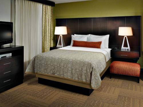 Staybridge Suites Miamisburg, an IHG Hotel في مياميسبيرغ: غرفة نوم بسرير ومصباحين وتلفزيون