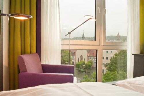 a bedroom with a purple chair and a window at B&F Hotel am Neumarkt in Bad Hersfeld