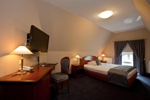 a hotel room with a bed and a desk and a television at Villa Knobelsdorff in Pasewalk