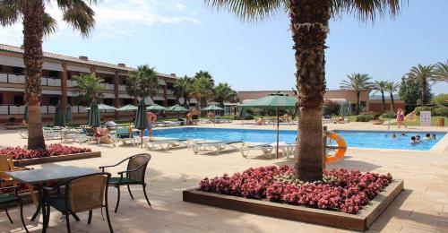 un complejo de piscina con mesas, sillas y palmeras en Hotel Clipper - EL DELFÍN VERDE RESORTS - Platja de Pals, en Torroella de Montgrí