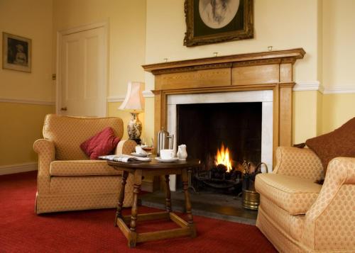 a living room with a fireplace with two chairs and a table at Worsley Arms Hotel in Hovingham