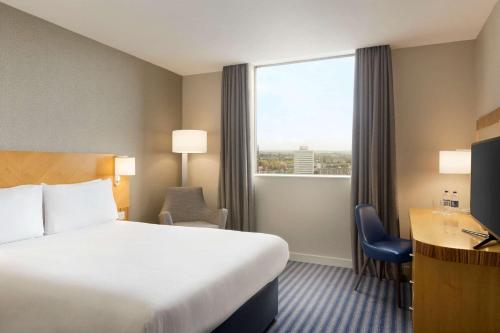 a hotel room with a bed and a desk and a window at Ramada Hotel & Suites by Wyndham Coventry in Coventry