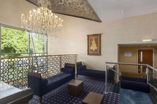 a lobby with blue chairs and a chandelier at Ramada Birmingham Oldbury M5 J2 in Oldbury