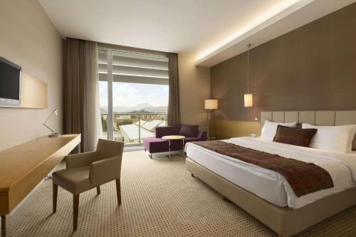a hotel room with a bed and a desk and a window at Ramada by Wyndham Podgorica in Podgorica