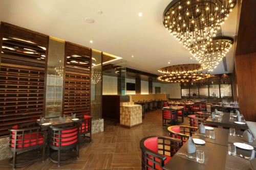 a restaurant with red chairs and tables and chandeliers at Ramada Encore Jalandhar in Jalandhar