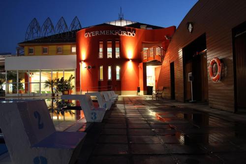 a building with benches in front of it at night at Colosseum Hotel in Mórahalom