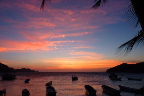 a sunset on a beach with boats in the water at Divanga Hostel and Diving in Taganga
