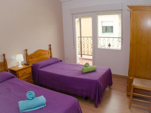 two beds in a room with purple sheets and towels at Hostal Los Calatravos in Alcañiz