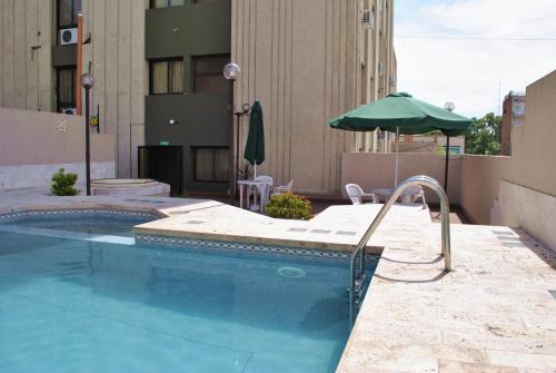 una piscina con una sombrilla verde junto a un edificio en Altezza Apart Suites en Mendoza