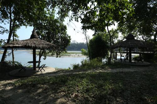 two picnic tables and umbrellas next to a body of water at Jungle Villa Resort - Near Chitwan National Park in Chitwan