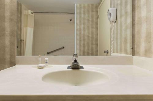 Travelodge by Wyndham Edmundston في إيدموندستون: حوض الحمام به صنبور ومرآة