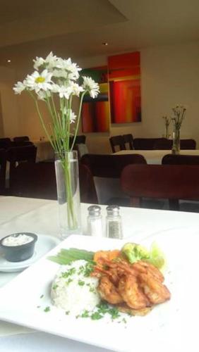 a plate of food on a table with a vase of flowers at Hotel Hex Estelí in Estelí