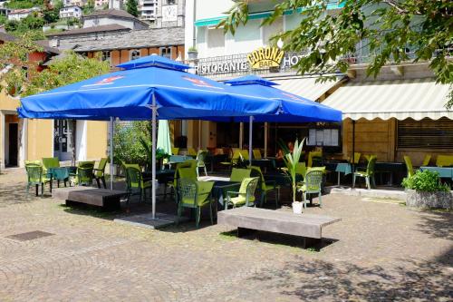 a patio with tables and chairs and blue umbrellas at Hotel Corona in Locarno