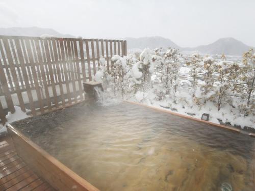 a hot tub on a deck with snow covered trees at Hotel Tsubakino in Yamanouchi