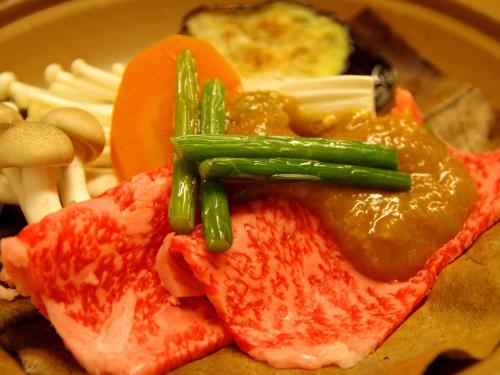 a plate of food with meat with sauce and asparagus at Gero Onsen Fugaku in Gero