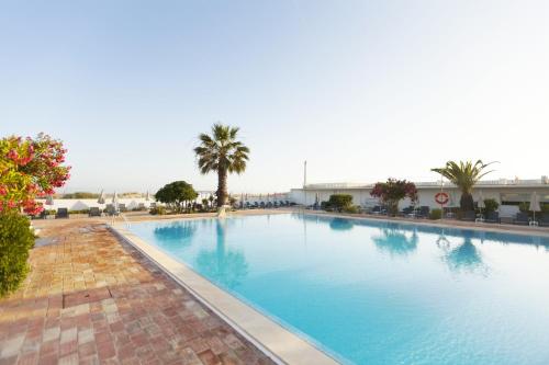 a large swimming pool with palm trees and a building at Hotel Vasco Da Gama in Monte Gordo